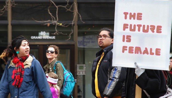 Several marchers in a street demonstration look at a sign one of them is carrying, which says, "The Future is Female"