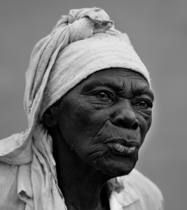 An elderly woman in a white turban purses her lips pensively as she seems to be watching some inner story