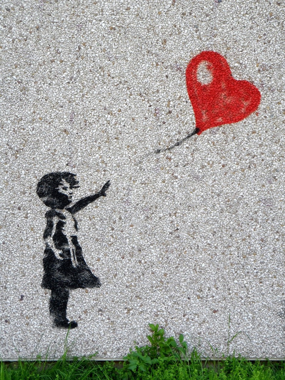 'Girl With Balloon' wall stencil by the artist Banksy showing a girl in black with her hand outstretched towards a a heart-shaped balloon flying just out of reach.