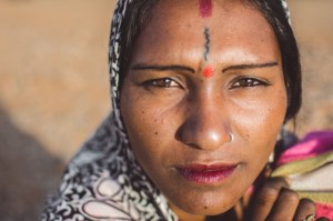 Woman with painted markings on her forehead and a nose ring, wearing a scarf over her hair.