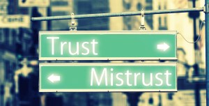 Two street signs are mounted on the same pole, pointing in opposite directions. One says "Trust" and the other says "Mistrust" 