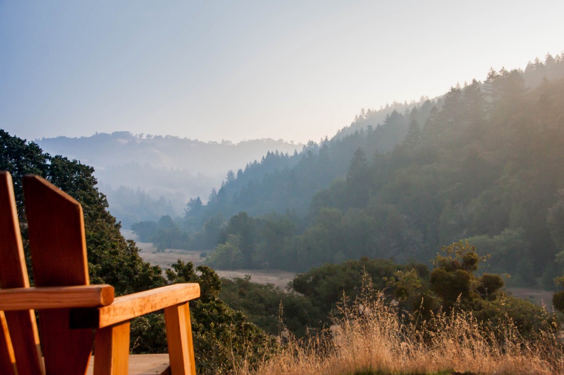 Looking over an Adirondack chair into a valley edged by wooded hills. 