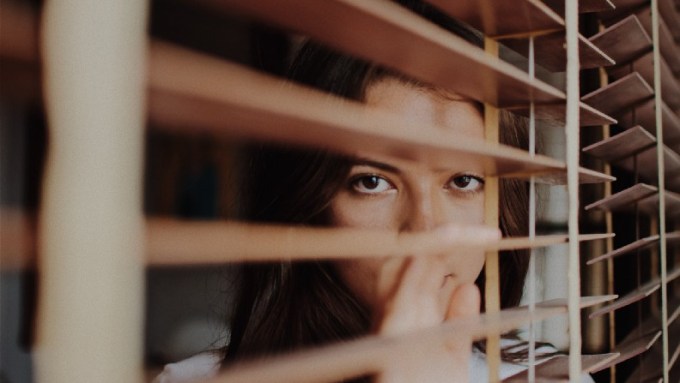 Woman peers through venetian blinds