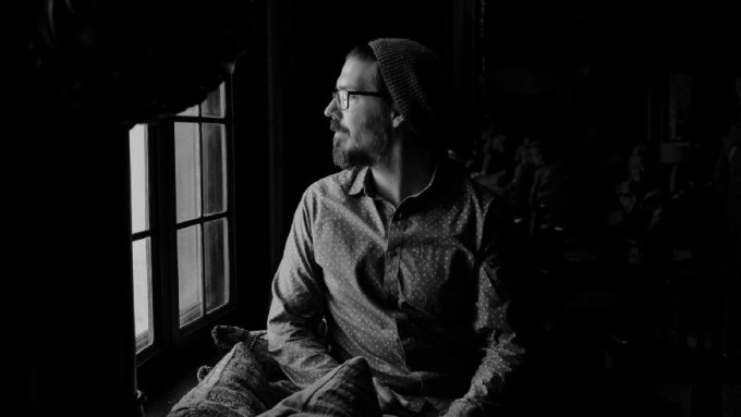 A man in a knit cap looks thoughtfully out a window - Image by Zachary Nelson (Unsplash)